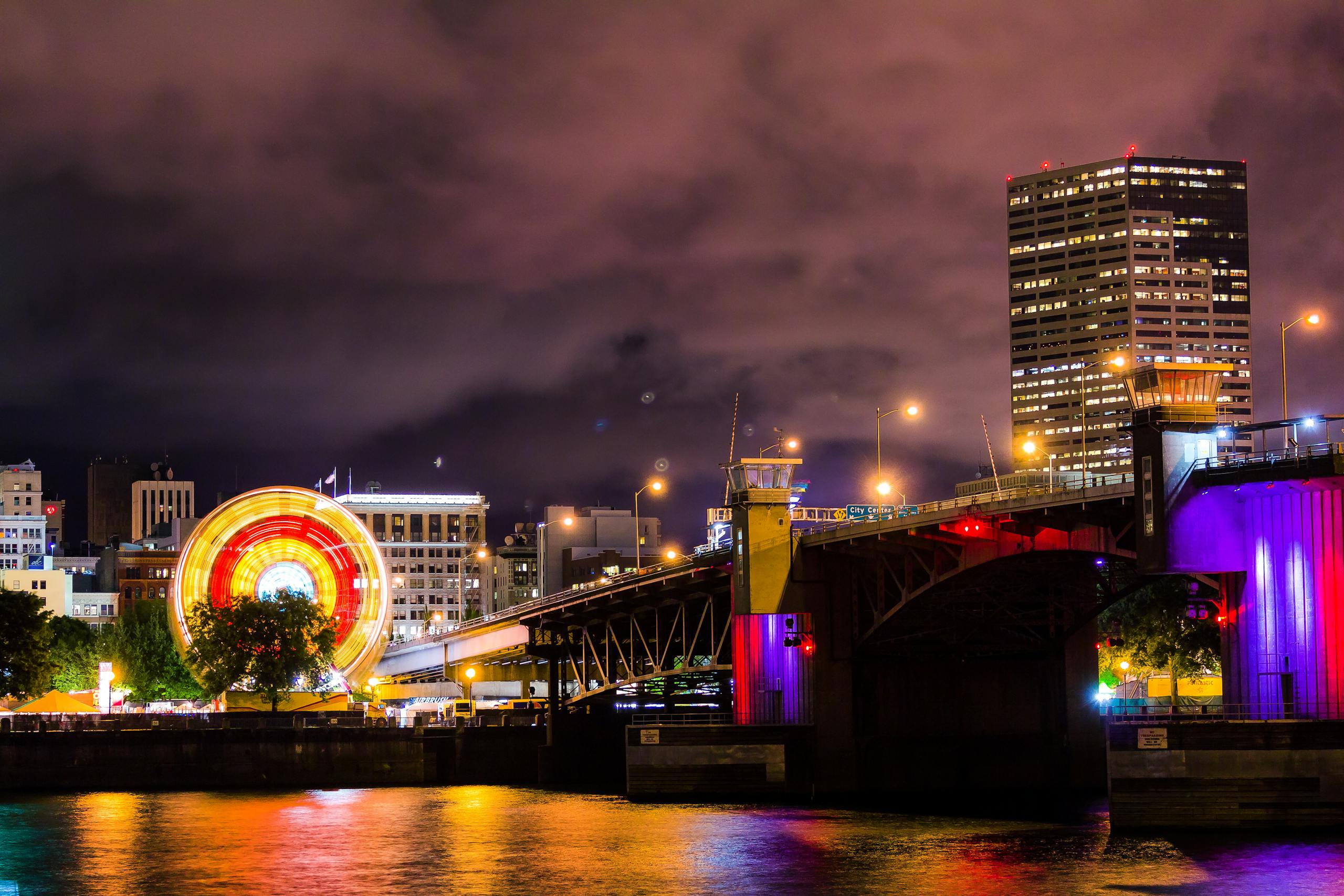 A night view of Portland's illuminated skyline featuring a ferris wheel and bridge reflection on the waterfront.