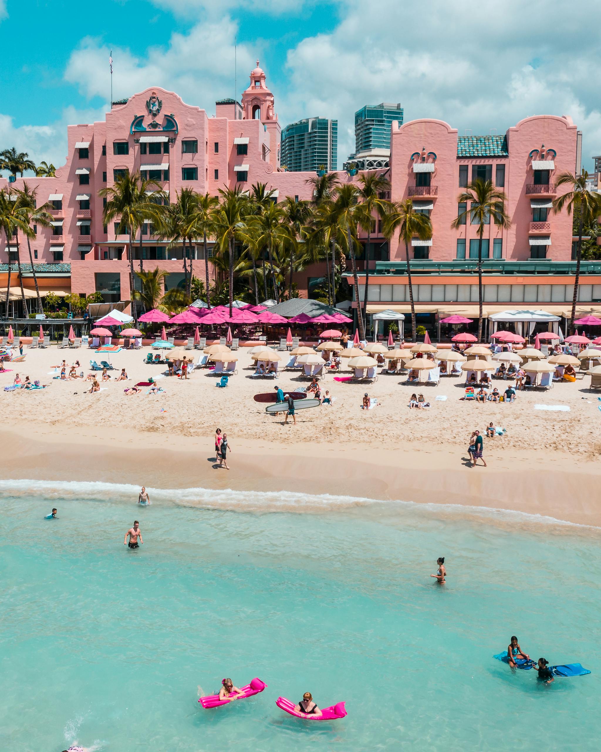Aerial view of Waikiki Beach with iconic pink hotel, palm trees, and ocean.